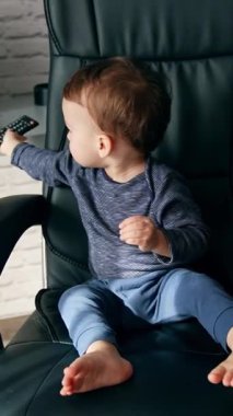 Yalınayak sevimli beyaz çocuk büyük deri koltukta rahatça oturuyor. Tatlı çocuk, arkasında duran dizüstü bilgisayara döner. Dikey video