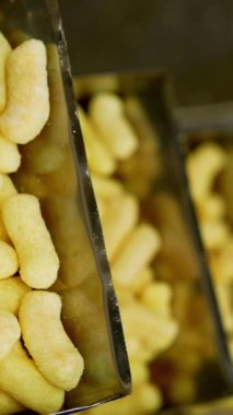 Çıtır mısırlı abur cubur üretiyor. Taşıyıcıda çıtır çıtır sarı patlamış mısır hareket ediyor. Dikey video