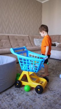 Turuncu tişörtlü çocuk arabaya doğru geliyor. Sevimli çocuk yerden oyuncakları topluyor ve tramvaya koyuyor. Dikey video.