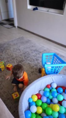 Küçük çocuk arabaya bir top attı. Bebek kuru havuza atlıyor ve zevkle yuvarlanıyor. Dikey video.