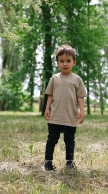 Küçük bebek parkta kuru çimenlerin üzerinde duruyor. Mutlu çocuk yazın doğada koşar. Dikey video.