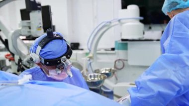 Cerrahi hoparlör takan ve hastaya bakan bir doktorun kafasından vurulmuş. Doktora yardım etmek ameliyatı izleyen hastanın üzerine eğilir..