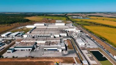 Modern bir fabrikanın bölgesine daha yakın uçmak. Hava perspektifinden, güneşli bir günde endüstriyel girişimin faydaları. Arkaplanda tarlalar ve ağaçlar.