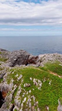 Deniz kıyısındaki resim gibi kayalar. Kanodaki bir insan kayaların altında kürek çekiyor. Su yüzeyinin üstü bulutlu. Dikey video.