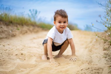 Çocuk açık havada güneşli bir günde kumda oynuyor. Genç bir çocuk, güneşli bir günün sıcaklığının tadını çıkararak, toprak bir patika boyunca kumlarda neşeyle oynuyor..