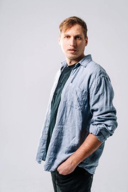 Genç adam rahat bir şekilde poz veriyor. Bir adam hafif bir arka plana karşı duruyor, sıradan bir tişört ve siyah tişört giyiyor, içsel bir ifadeyle..