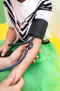Çocuk sağlık kontrolü yaptırıyor. Renkli bir klinikteki rutin sağlık kontrolünde bir çocuğun tansiyonu kontrol ediliyor..