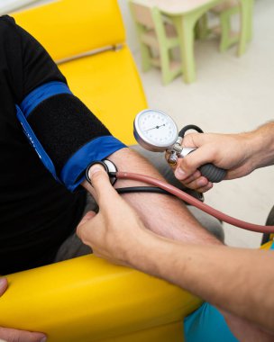 Hastayla klinik bir ortamda sağlık kontrolü. Parlak bir sağlık tesisinde, siyah gömlekli bir insan tansiyon ölçümünden geçiyor..