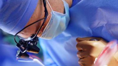 Cerrahın ameliyat lenslerini takması hastaya yakındı. Doktor metal alet ve elektrikli cihaz uygulamak için çaba sarf ediyor. Kapat..