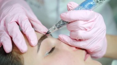 Ustanın elleri, kaş dövmesini iğne makinesiyle yapıyor. Kapatın. Modern kalıcı kardeş makyajı..