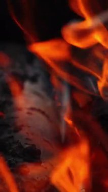 Yanmış ahşap kütüklerin arka planı. Yanan ağaçtan beyaz kül. Kömürlerin üzerinde hafif alevlerin detaylı hareketi. Yakın plan. Ağır çekim. Dikey video