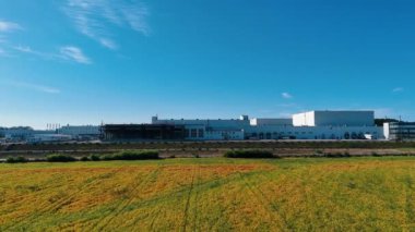 Sarı tarlanın üzerinde uçan büyük fabrikaya yaklaşıyoruz. Mavi gökyüzünün arkaplanındaki modern girişimin dışı..