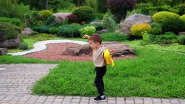 Sarı kazaklı şirin çocuk topu fırlatıyor. Küçük çocuk yazın güzel parkta yürüyor..