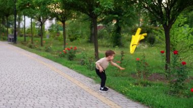 Beyaz çocuk sarı kazağını çimlere ve güllere fırlatıyor. Gülümseyen çocuk kıyafetlerini seçmeye gidiyor..