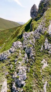 Güneşli bir günde ulaşılamayan kayaların üstündeki insansız hava aracı görüntüleri. Bazı turistik yerler dağların eteklerindedir. Dikey video.