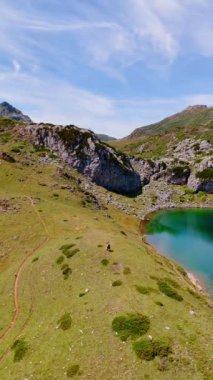 Çift güzel gölün üzerindeki tepede duruyor. Güneşli bir günde, dağlık bölgede insansız hava aracı görüntüleri. Dikey video.