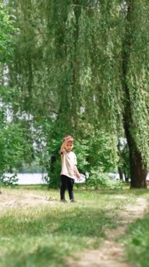 Tatlı erkek bebek söğüt ağacının yanında duruyor. Küçük çocuk elini sallıyor ve bir huş ağacına doğru yürüyor. Dikey video.