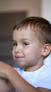 Bıyıklı, içkiden çıkmış güzel bir beyaz çocuk. Şirin çocuk yemeğini çiğneyip ellerini çırpıyor. Kapatın. Dikey video.