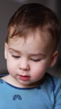 Mavi tişörtlü şirin beyaz çocuk oyuncaklarla oynuyor. Küçük bir erkek bebeğin bir oyuna odaklanmış portresi. Kapatın. Arkaplan bulanık. Dikey video