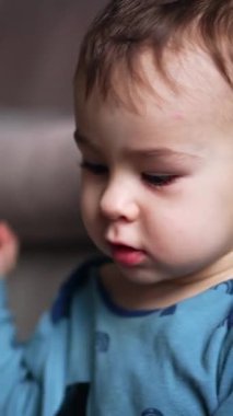 Beyaz, tatlı erkek bebek içeride oturuyor. Sevimli çocuk elini göğsünden alkışlıyor. Kapatın. Arkaplan bulanık. Dikey video