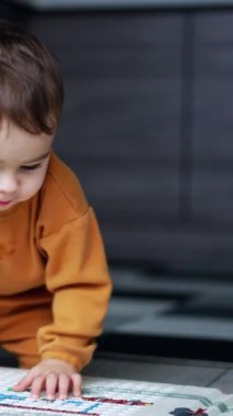 Yerde sürünen ve halıya dikkatlice bakan küçük tatlı bir oğlan çocuğu. Küçük çocuk içeride oynuyor. Arkaplan bulanık. Dikey video