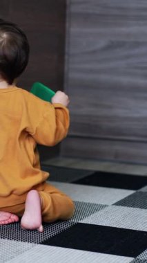 Koyu saçlı bebek yerde oturuyor. Sırtı kameraya dönük. Bebek çekmeceyi ileri geri çeker ve konteynır kapağıyla oynar. Dikey video