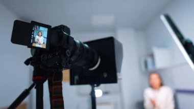 Bir blog için video içeriği oluşturuluyor. Kamera bir kadının masada oturup konuştuğunu kaydediyor. Bulanık arkaplan.