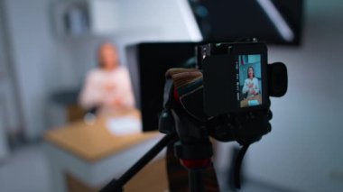 Esmer, uzun saçlı bir kadın kameraya konuşuyor bir elini göğsüne dayayıp diğeriyle el kol hareketi yapıyor. Bir günlük için kayıt videosu.