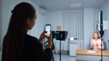 Kadınlar içeride çalışır ve video çeker. Bir bayan akıllı telefonuyla bir video kaydediyor ve diğeri bir konuşma yapıyor..