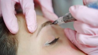 Dövme makinesi müşterinin kaşları tarafından hızla hareket ettirildi. Mikro patinaj ve kalıcı makyaj. Kapat..