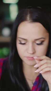 Ekose gömlekli güzel bir kadın arka plandaki kafede meyve suyu içiyor. Dikey video