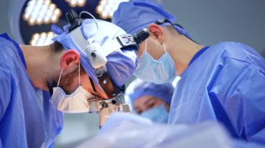Beyin cerrahı hastanın ameliyatının üzerine eğildi. Ameliyatta cerrahi hoparlörlerde odaklanmış iki doktor..