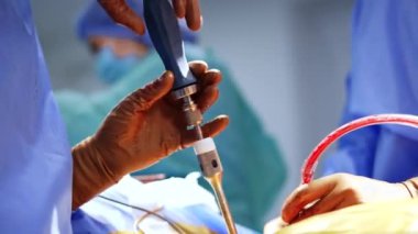 Doktorun elleri kahverengi lateks eldivenlerle kana bulanmış ve ameliyat sırasında tornavida kullanıyor. Doktora yardım etmek kan emici bir alet. Kapat..