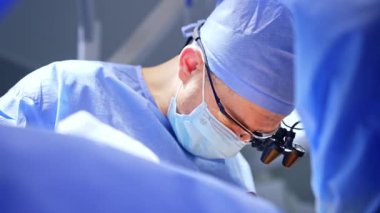 Maskeli, kepli ve cerrahi burunlu beyaz erkek cerrah. Operasyonu yürüten doktora alçaktan bakış açısı.