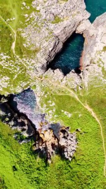 Uçsuz bucaksız kayalar ve akan mavi su. Dağın düz tepesini yeşil çimenler kaplıyor. Turist yollarıyla kesişiyor. Üst Manzara. Dikey video.