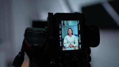 Kameradaki ekran, uzun saçlı kadının konuştuğunu gösteriyor. Stüdyoda bir blog içeriğinin görüntüsü. Kapatın. Bulanık arkaplan.