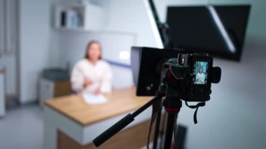 Tripodun üzerindeki kamera bir kadının konuşmasını kaydediyor. Blog için içerik oluşturuluyor. Bulanık arkaplan.