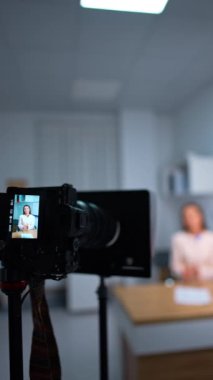 Esmer kadın bir odada masa başında kamerayla konuşuyor. Blog içeriği kaydediliyor. Arkaplan bulanık. Dikey video.