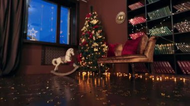 Odanın köşesindeki güzel dekore edilmiş Noel ağacına yaklaşıyoruz. Ağacın yanında rahat bir kanepe ve sallanan at. Yerdeki ışık çelenklerini açtı. Düşük açı görünümü.