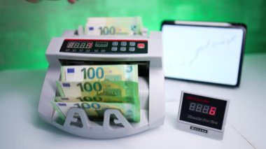 Para sayma makinesi masanın üstündeki stantları açtı. El, 100 avroluk banknotlara dokunuyor ve onları sayıyor. Kapat..