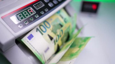 Para sayma makinesinin kılıçları boş dönüyor. Yeşil 100 avroluk banknotlar sahibine düşer. Kapatın. Bulanık arkaplan.