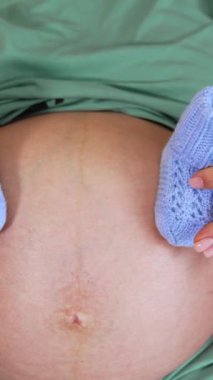 Yeni doğmuş bebek poposu olan hamile bir kadın göbeği. Yatağında bebek aksesuarları olan hamile bir kadın. Kapatın. Dikey video