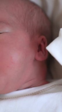 Tapılası yeni doğmuş bebeğin yüzü. Evdeki yatakta duran sağlıklı, tatlı bir çocuk portresi. Mutlu bir aile ilişkisi ve yeni doğmuş bir bebek. Yakın plan dikey video.