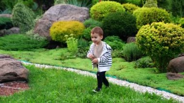 Çimlerin üzerinde zıplayan neşeli beyaz çocuk. Mutlu çocuk güzel parkta vakit geçiriyor..