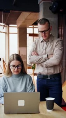 Erkek ve bayan meslektaşım ofiste. Bayan dizüstü bilgisayarında çalışıyor. Adam yanında durup kadınla konuşuyor. Dikey video