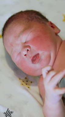 Eldivenli doktor steteskoplu bir bebeği dinliyor. Çıplak bebek el sallıyor. Üst görünüm kapalı. Dikey video