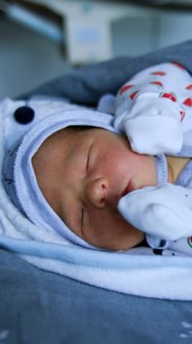 Şapkalı küçük tatlı bir bebek ve uyuyan eldivenler. Yatakta battaniyeli küçük bir bebek. Kapatın. Dikey video