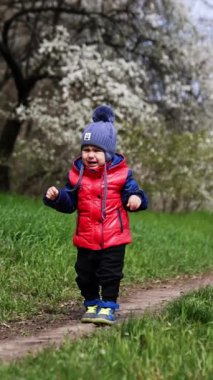 Sevimli erkek bebek mutsuz ve yolda inliyor. Baharda yürüyüşe çıkan küçük bir çocuk. Dikey video