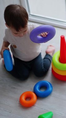 Sevimli beyaz çocuk dizlerinin üstüne çöküp yere oturuyor. Çocuk piramidi balkona inşa ediyor. Yukarıdan bak. Dikey video