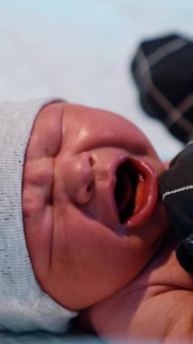 Şapkalı ve eldivenli yeni doğmuş bebek acı acı bağırıyor. Sıhhiyeci çocuğun bezini bağlıyor. Kapatın. Dikey video